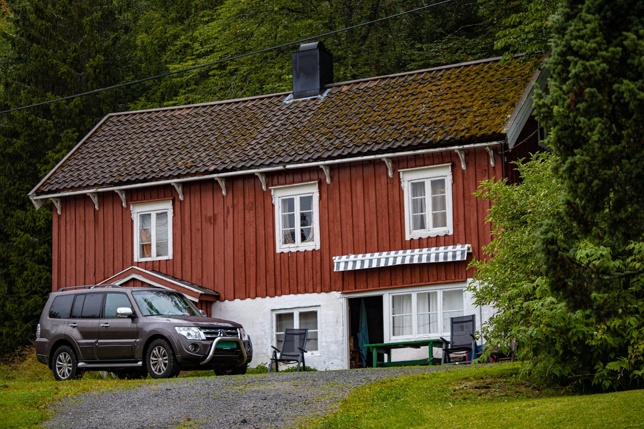 Charming rustic cabin with a car parked beside, set amidst lush greenery in summer.